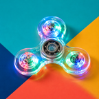 A three-spoke transparent fidget spinner with glowing multicolor LED lights, centered on a diagonally split teal, orange, and dark blue background.