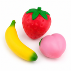 Three soft, squishy toy fruits on a plain white background: a red strawberry with green leaves, a yellow banana with a green tip, and a pink peach with a small green stem.